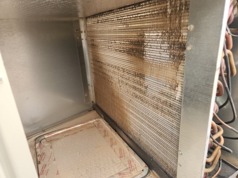 Interior of air conditioning unit showing dirty mesh filter with dust accumulation and debris on the floor