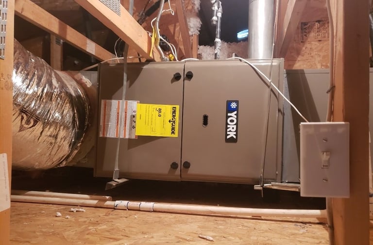 Tan HVAC furnace unit with yellow warning label installed in basement with ductwork and copper piping