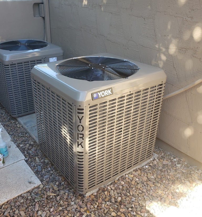 Two outdoor YORK air conditioning units installed on gravel ground against a brick wall