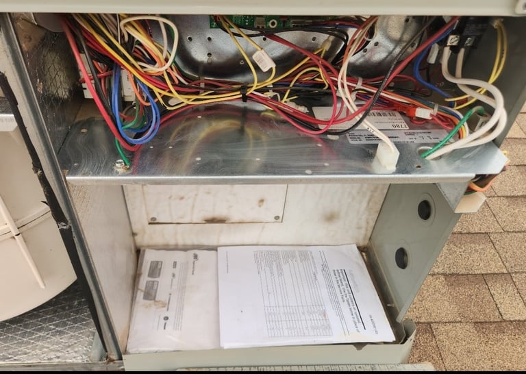 Interior of HVAC unit showing tangled colored wires, components, and documentation sheets on bottom panel